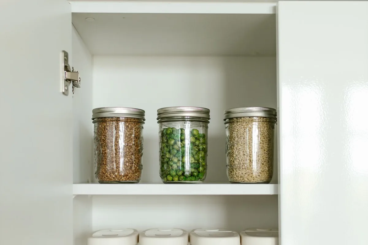 An open white cabinet in a Newport Beach CA kitchen showing a concealed hinge and storage jars on the shelf