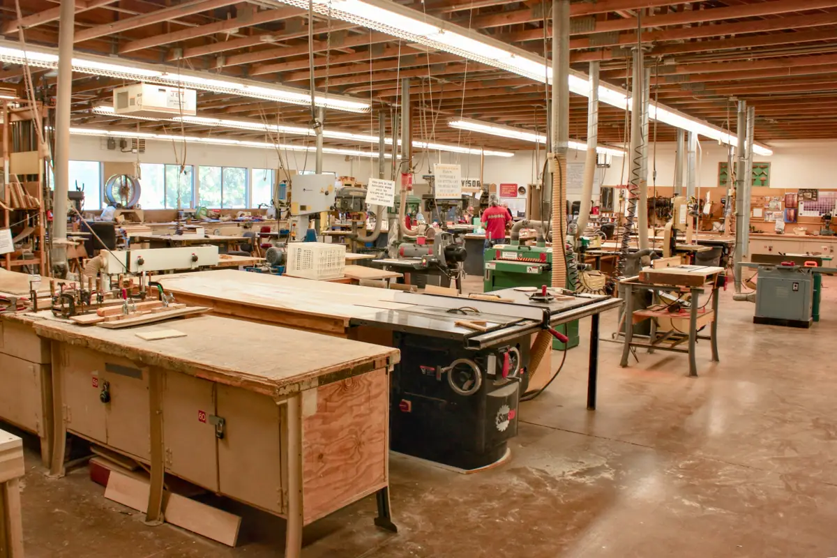 A cabinet shop floor with a table saw, jointer and assembly benches under overhead dust extraction